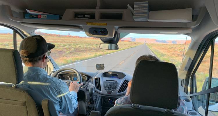 View from inside a vehicle with passengers traveling on a desert highway.