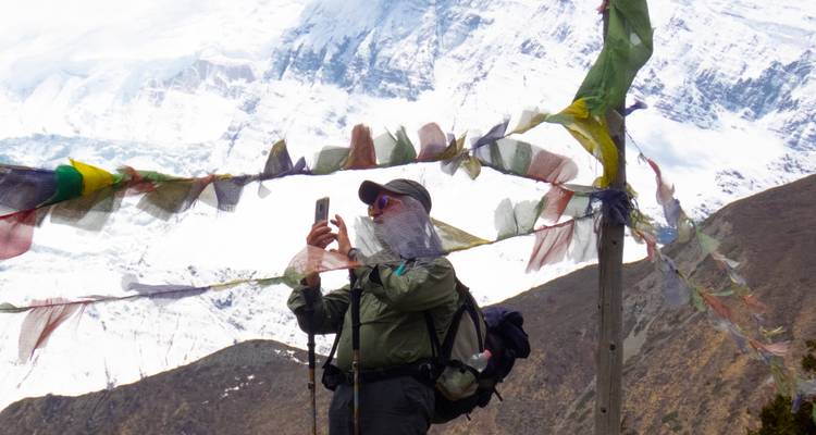 Hiker taking a photo among prayer flags with snow-covered mountains in the background.