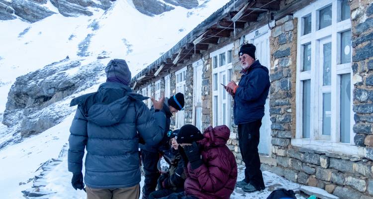 Group of hikers resting by a stone building in a snowy mountain landscape.