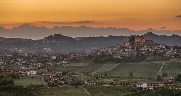 Weitläufiger Sonnenuntergangsblick über sanfte Weinberge und eine Bergstadt mit Alpengipfeln am Horizont