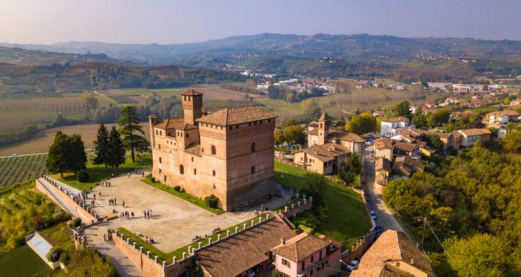 Drohnenaufnahme des roten Backsteinschlosses Grinzane Cavour, umgeben von Landschaft und Dörfern
