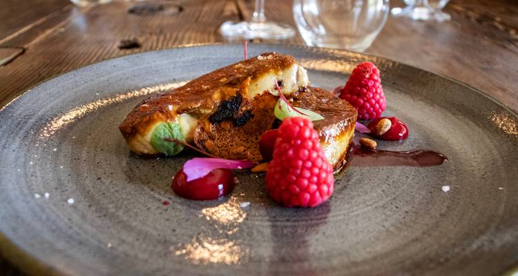 Un plato gourmet de foie gras caramelizado adornado con frambuesas frescas y salsa descansa sobre una mesa de madera rústica.