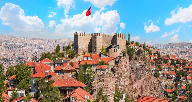 Turkse vlag wappert boven stenen muren van het kasteel van Ankara met uitzicht op huizen met rode daken en stadslandschap.