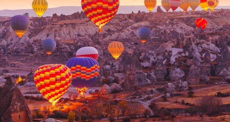 Tientallen kleurrijke heteluchtballonnen zweven boven Cappadocië's surrealistische rotslandschap bij zonsopgang.