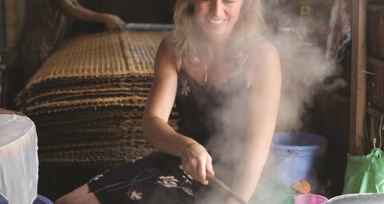 A woman cooking in a local market setting with steam rising.