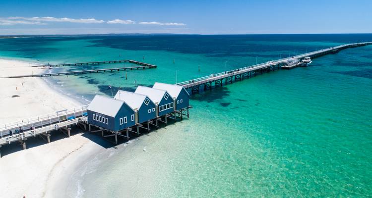 Aguas turquesas y arenas blancas en el Muelle de Busselton con casetas de botes azules que se extienden hacia el mar.