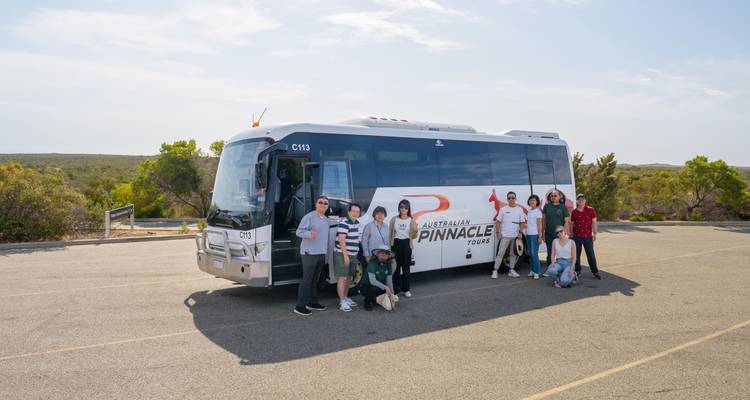 Grupo de tour posando al lado de un autocar de Australian Pinnacle Tours en un soleado estacionamiento.