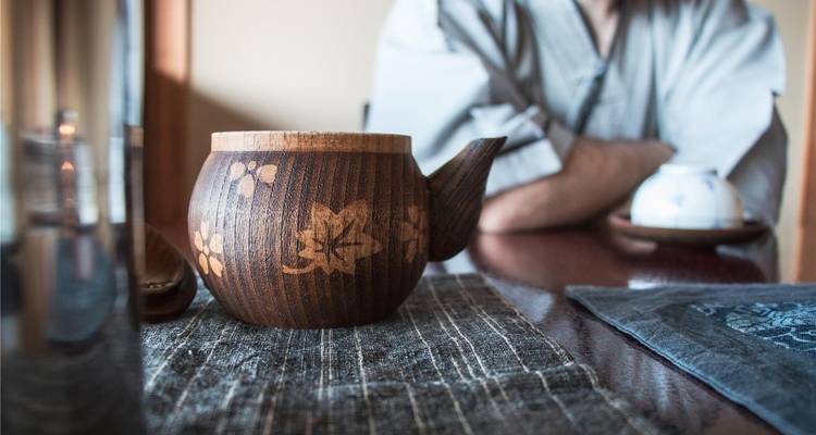 Una tetera de madera rústica con tallado floral descansa sobre una estera tejida durante una tranquila ceremonia del té.