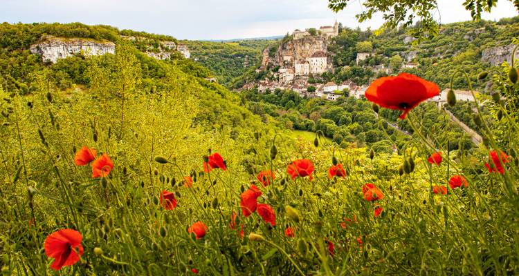 Las amapolas rojo brillante enmarcan un pueblo en lo alto de un acantilado a lo lejos, posado bien alto sobre un valle verde en Francia.