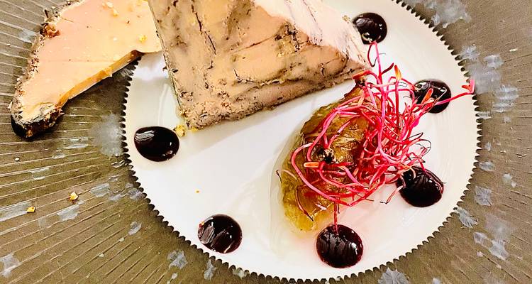 Un elegante plato de foie gras presentado con compota de frutas, puntos de salsa y microvegetales de colores.