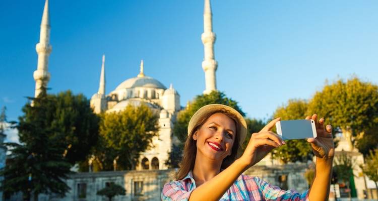 Mujer tomándose una selfie con una mezquita de fondo.