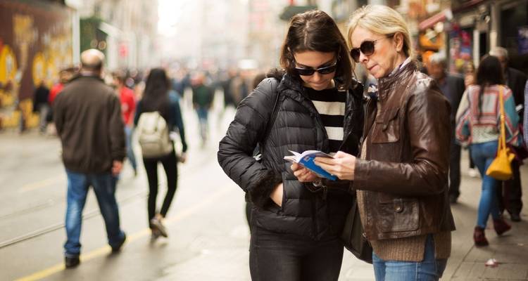 Dos mujeres mirando una guía turística en una calle concurrida.