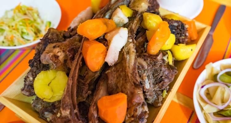 Traditionelle Mahlzeit mit Fleisch und Gemüse serviert auf einer Holzplatte.