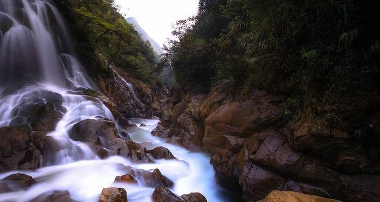 Serener Wasserfall, der über Felsen kaskadiert, umgeben von üppiger Vegetation.