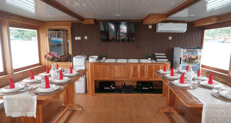 Salle à manger intérieure soignée sur un bateau en bois dressée pour un repas avec des serviettes à pointes rouges.