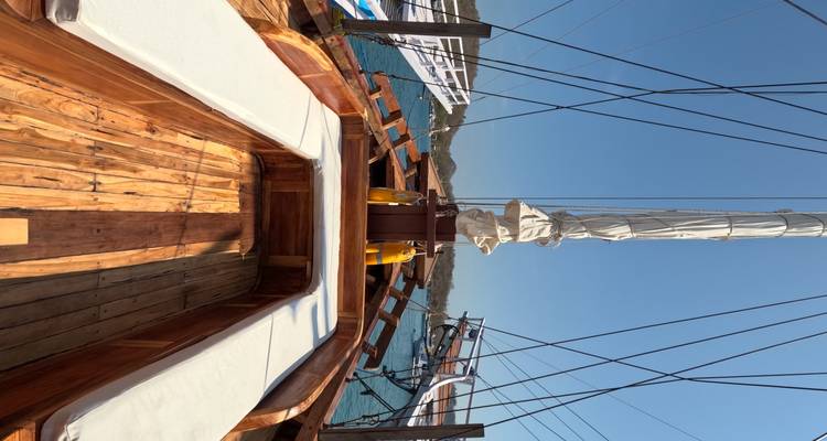 Pont avant ouvert d'un voilier en bois avec des bancs rembourrés regardant vers le mât sous un ciel dégagé.