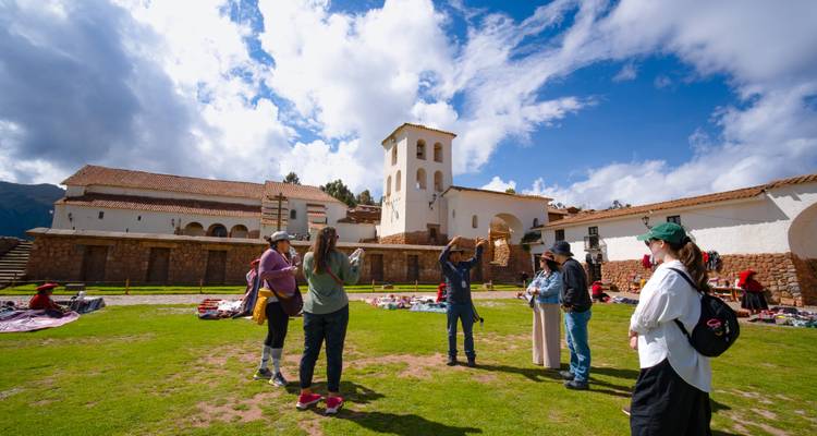 El guía señala a los visitantes en el patio de pasto del complejo de la iglesia de Chinchero bajo unas nubes dramáticas.