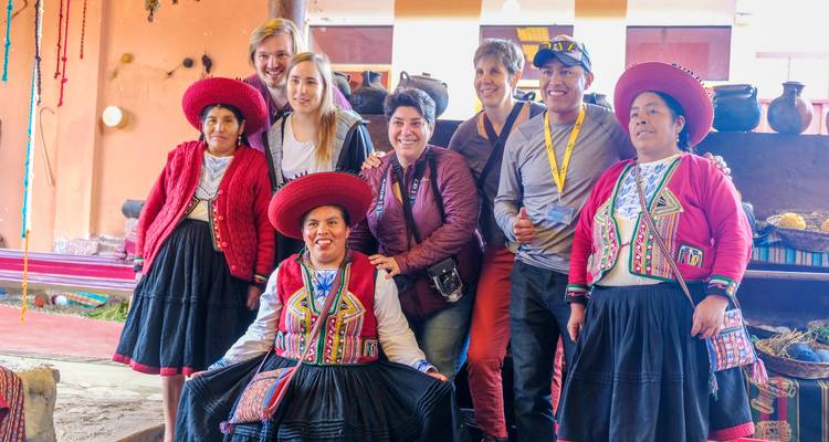 Los viajeros posan felices con mujeres quechuas que usan sombreros rojos tradicionales y faldas bordadas dentro de un taller de tejido.