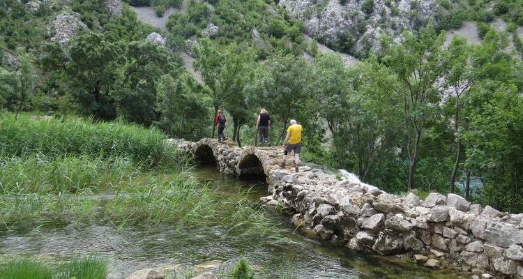 Plusieurs personnes marchant sur un pont de pierre dans une région montagneuse.