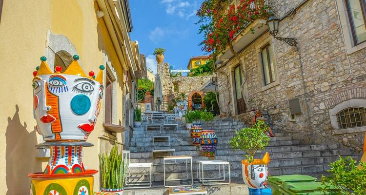 Jarrones de cabeza cerámica pintados con colores brillantes decoran una estrecha escalera de piedra en un encantador callejón mediterráneo bajo un cielo azul.