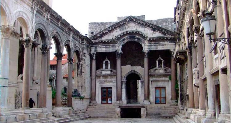 Patio con columnata de piedra del Palacio de Diocleciano con arcos de mármol desgastado y pocos visitantes.