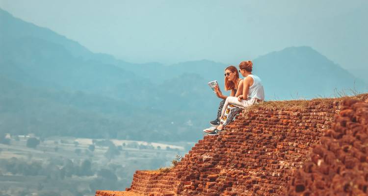Deux personnes assises sur des ruines avec vue sur les montagnes.