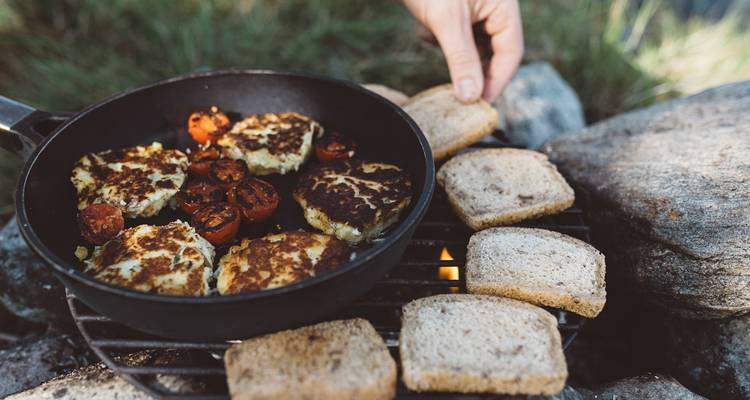 Personne cuisinant des tomates et du pain sur un feu de camp.