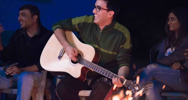 Gitarre spielende Person am Lagerfeuer mit Freunden in der Nähe.