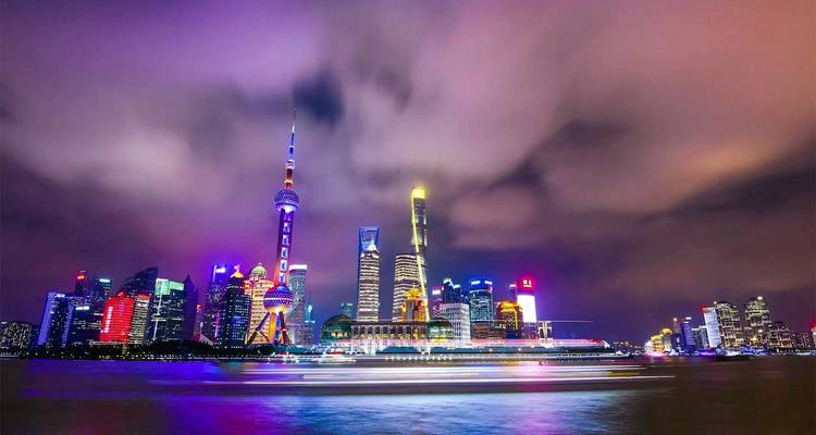 Vista nocturna de larga exposición del horizonte iluminado de Shanghai con un crucero desenfocado en el río Huangpu.