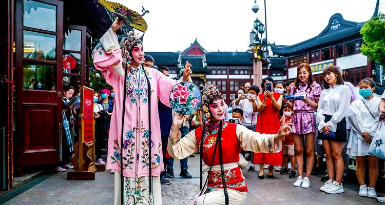 Les interprètes d'opéra de rue vêtus de costumes ornés divertissent une foule animée dans un cadre de vieille ville.