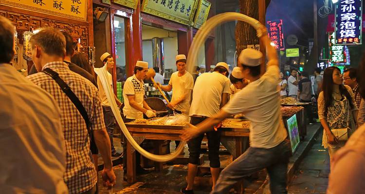 Nachtmarktscène in Xi'an met koks die noodels met de hand trekken tussen neonborden en nieuwsgierige toeschouwers.