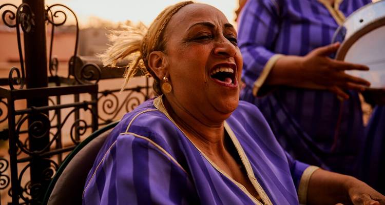 Local Moroccan woman in purple kaftan laughs heartily during an evening gathering.
