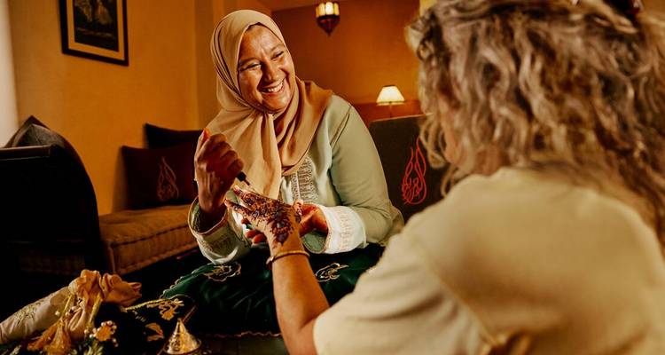 Host demonstrates traditional henna art to an intrigued traveller inside a Moroccan riad.