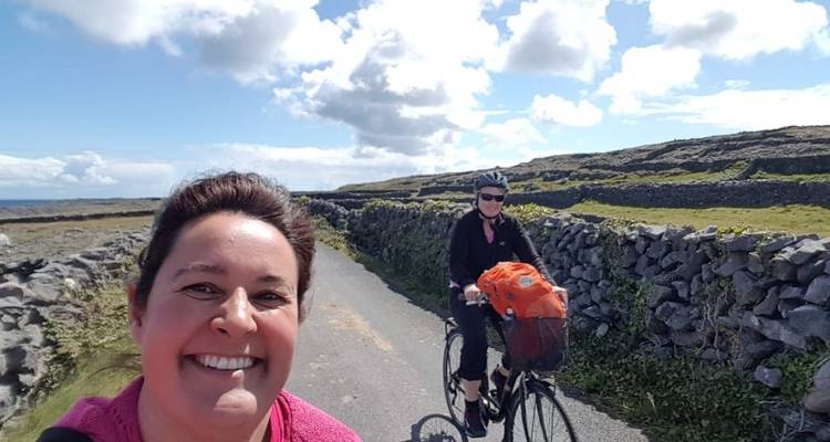 Femme souriante avec un cycliste en arrière-plan sur une route de campagne.