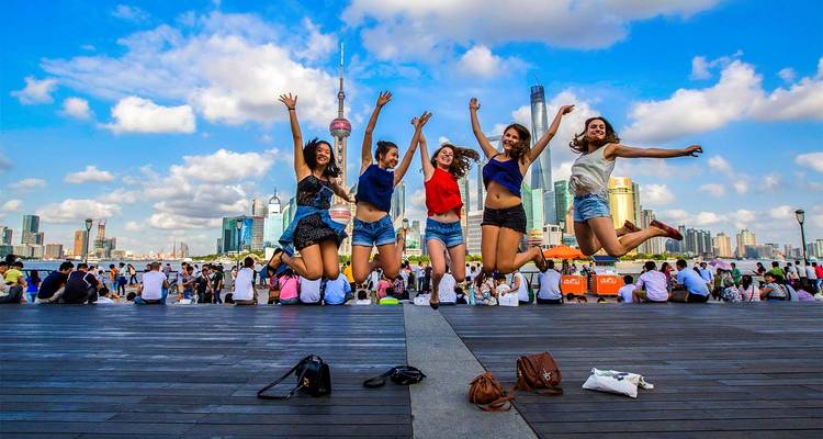 Cinco amigos saltan alegremente para una foto en el Bund de Shanghái con el skyline futurista de fondo.