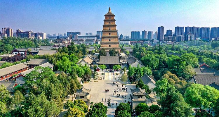 Perspectiva aérea de la Gran Pagoda de la Oca Salvaje de Xi'an elevándose sobre los terrenos del templo lleno de vegetación con el horizonte de la ciudad moderna más allá.