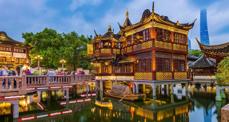 Los tradicionales edificios de madera del bazar del Jardín Yu de Shanghái brillan al atardecer junto a estanques reflectantes.
