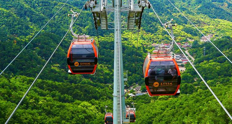Bright orange cable cars glide above lush green mountains providing panoramic valley views.