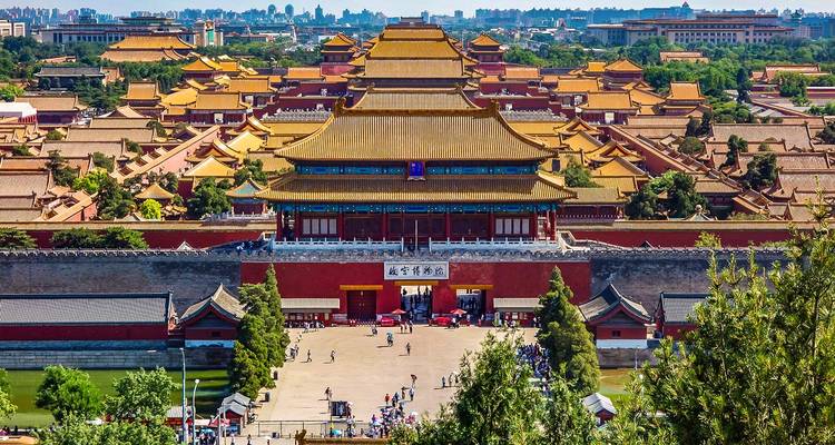 Elevated view of the Forbidden City’s golden roofs stretching toward modern Beijing in the distance.