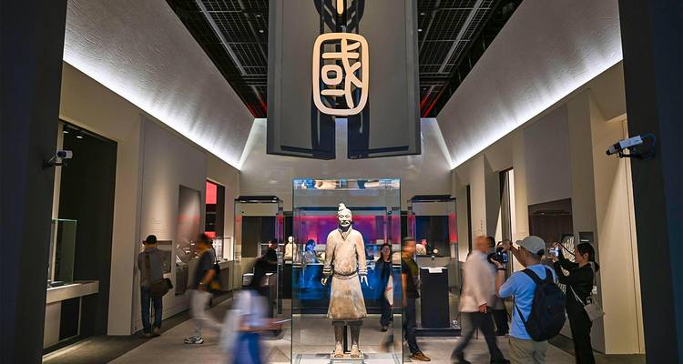 Modern museum exhibition hall with spotlighted terracotta warrior statue and blurred visitors passing by.