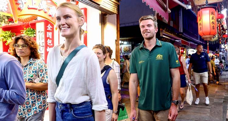 Foreign tourists explore a vibrant night market street lined with neon signs and lanterns.
