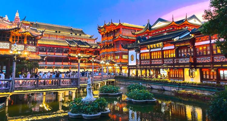 Evening lights illuminate the traditional pavilions and bridges of Shanghai’s Yu Garden over reflective ponds.