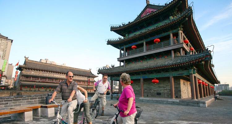 Turistas paseando en bicicleta junto a la muralla de la ciudad de Xi'an con faroles rojos.
