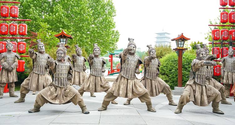 Des artistes de rue vêtus en guerriers en terre cuite adoptant des poses dramatiques dans une place extérieure.