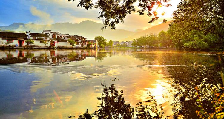 Vue panoramique d'un village avec un lac et une montagne au coucher du soleil.