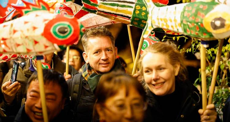 Vrolijk publiek dat kleurrijke papieren vislanterns draagt tijdens een nachtelijke festivaloptocht in China.