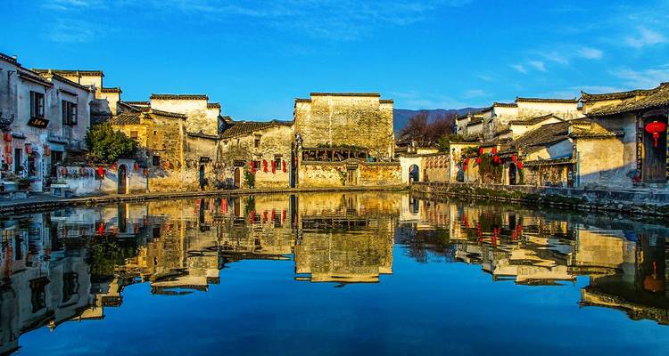 Spiegelglad weerspiegeling van oude Huizhou-architectuur rond een rustige waterplaats onder een levendige blauwe hemel.