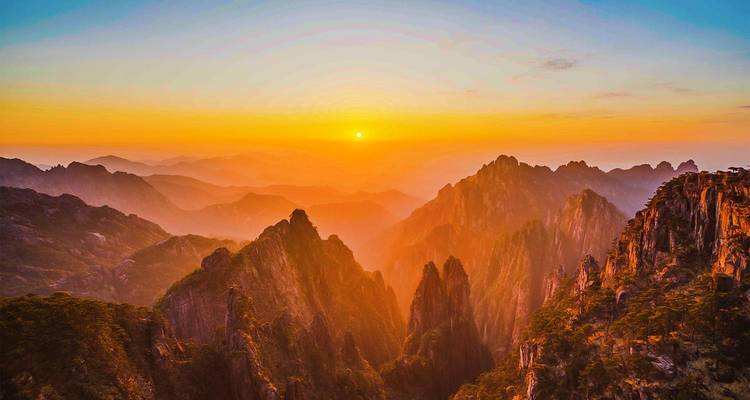 Vurige zonsopgang werpt gouden licht over de gelaagde bergkammen van Huangshan en creëert een dramatisch, mistig uitzicht.