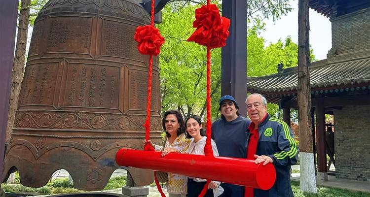 Four tourists pose beside a huge inscribed temple bell decorated with bright red ribbons.