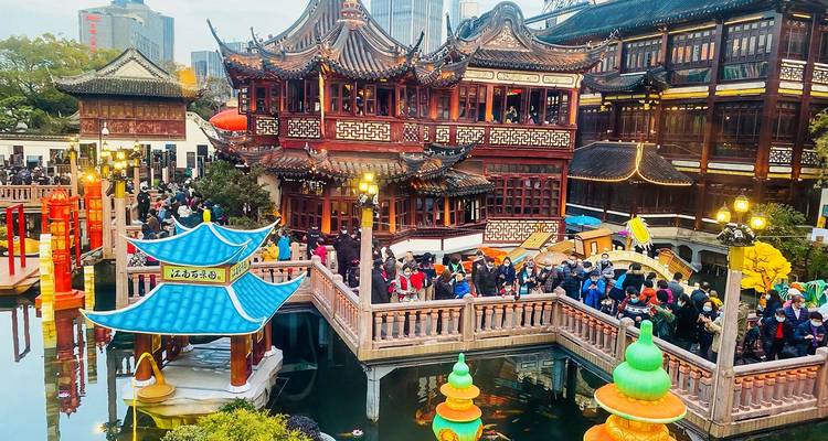 Menigten vullen de bruggen en wandelpaden van Yuyuan Bazaar tussen sierlijke traditionele gebouwen en lantaarns in de schemering.